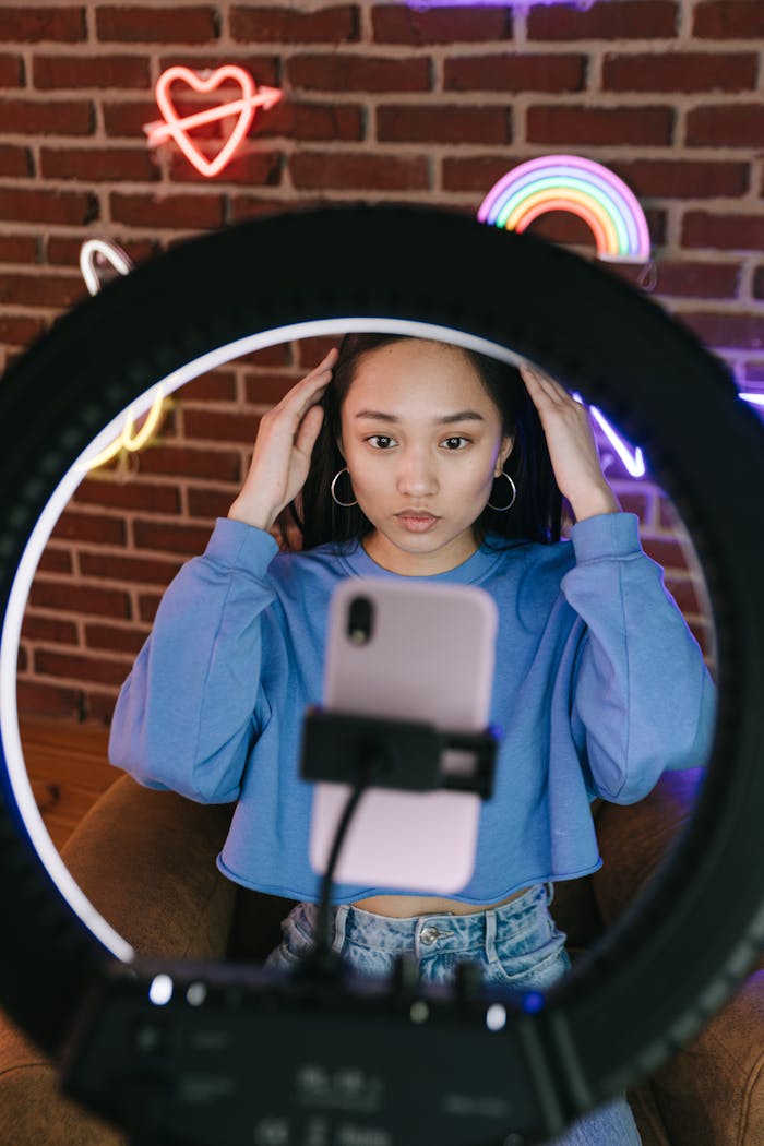 About Asian woman recording a video with a smartphone and ring light for streaming purposes.