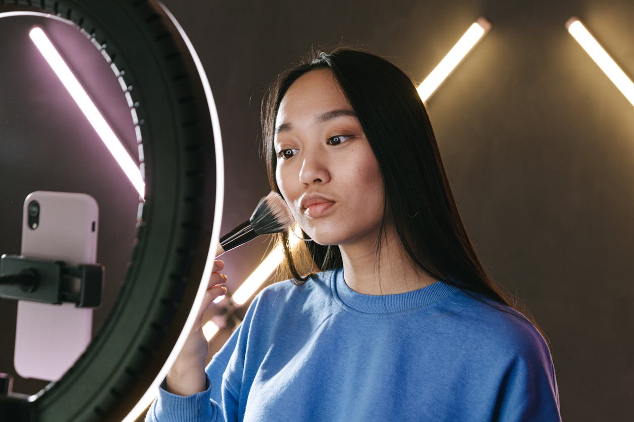 Asian woman filming a makeup tutorial for her vlog using a ring light, emphasizing beauty and creativity.